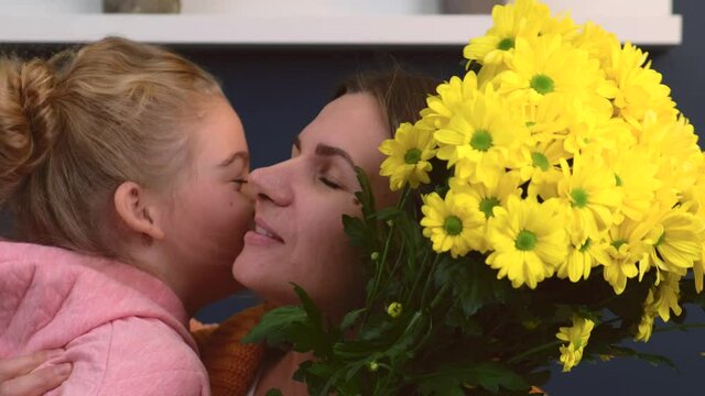 Caucasian mother and daughter are embracing with a bunch of flowers smiling and kissing each other