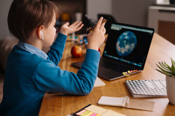 Fototapeta na wymiar A Preteen boy uses a laptop to make online classes, globe on the screen, making notes