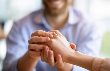 We are getting married. Happy fiance holding his future wife's hand with engagement ring on finger, cropped view