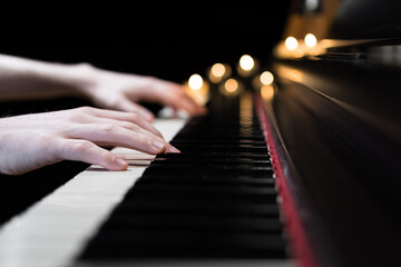 Hands playing the piano keyboard closeup and candle light bokeh background. Male pianist learning to play the piano instrument and beautiful music