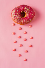 Vegan pink donut with hearts and sprinkles on pink background with pink glaze