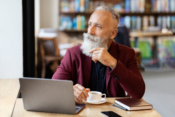Thoughtful senior man sitting at cafe, using laptop