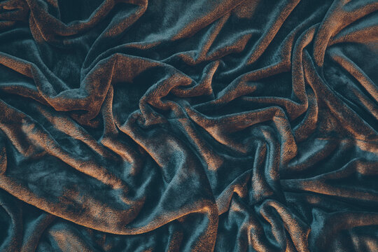 Detail of draped and crumpled velvet fabric, moody warm lighting illuminating wrinkles and creases