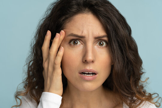 Close Up Of Worried Woman Without Makeup Has Signs Of Aging Skin, Checking Crows Feet Troubled With Wrinkles On Face, Afraid Of Getting Old, Looking At Camera, Isolated On Studio Blue Background. 