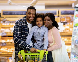 Happy black family with shopping cart purchasing food at supermarket