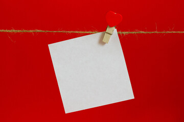 white sheet for notes on a red background with a clothespin with a heart on a whip rope for...