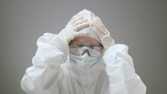 Exhausted Woman Taking Off A Protective Face Mask And Costume To Go To The Patients With Virus Infection, Pandemic Time. Female Preparing To Go Into The Laboratory To Research And Invet Treatment From