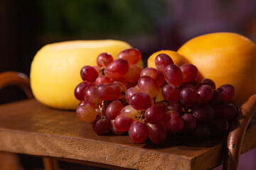 Bunch of grapes on a wooden board with cheeses in the background.
