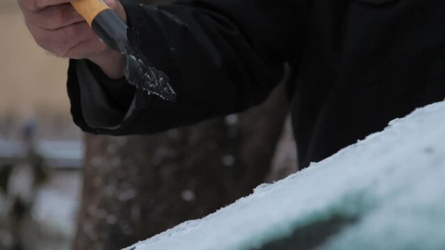 Person hand cleans electrocar windshield with rubber ice scraper of black and orange colours on cold day slow motion