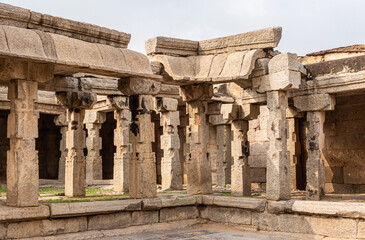 Obraz premium Hampi, Karnataka, India - November 5, 2013: Sri Krishna temple in ruins. Beige stone pillars and beams at a ruinous corner of the premises under light blue sky. Some grass.