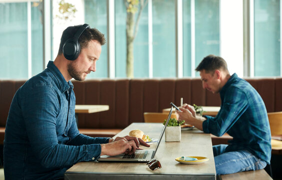 Two men seated in a cafe, working remotely  using a  laptop and smart phone