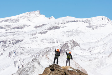 Two hikers up on a rock contemplating the landscape of the Sierra Nevada mountains with snow.