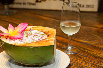 Thai ceviche served inside fresh coconut. Harmonized with a glass of white wine in the background