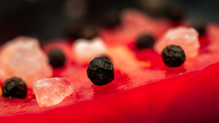 Plasterek pomidora okraszony ziarnem pieprzu i kryształem himalajskiej soli. Zdjęcie obiektywem makro. 