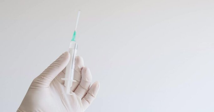 Doctor hand with medical glove holds and shakes syringe. Covid-19, Coronavirus vaccination concept, medical, treatment, looping video, space for text.