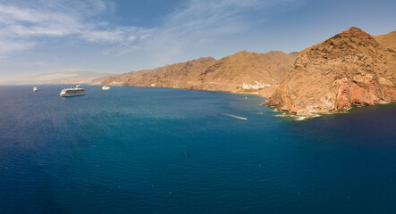 Anchoring cruise ships lie in front of St. Andres on the wild east coast of the Spanish Atlantic island of Tenerife. An aerial view from the sea side shows the town and the mountains in the background