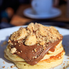 Vertical closeup view of pancakes with chocolate sauce on a white plate. Blur coffee shop background.