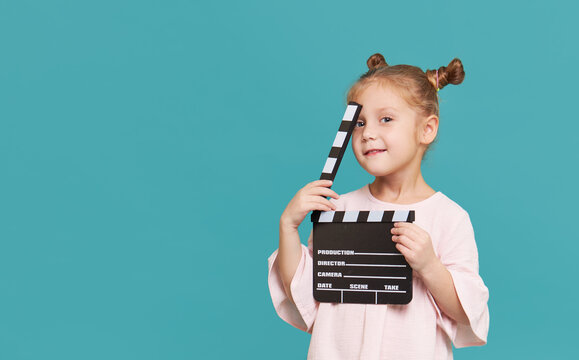 Funny smiling child girl hold film making clapperboard isolated on blue background. Little clipmaker, acting training. Funny face. Copy space for text..