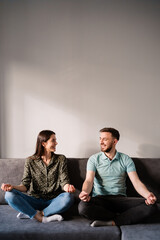 Young couple practicing meditation while sitting on gray sofa at home