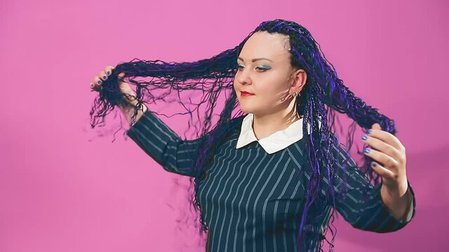 A stylish brunette with blue afro braids is fingering her strands with her hands. Medium plan