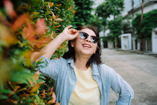 Portrait of senior woman wearing sunglasses standing by plant wall.