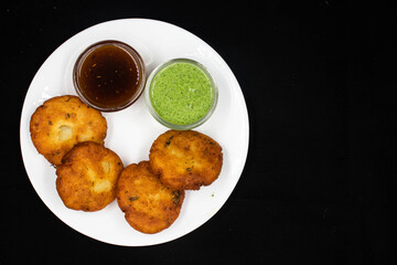 Indian Side Dish Popular Chaat Snacks Aaloo Aalu Mashed Boiled Potato Tikki With Spicy Green Chutney And Tomato Sauce On Black Background