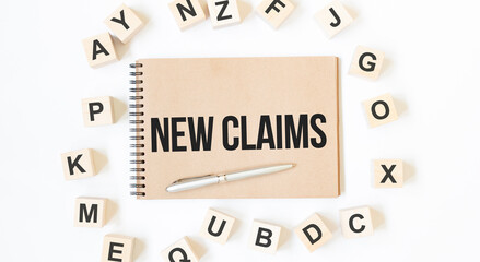 Text NEW CLAIMS on the craft colored notepad with block wood cubes on the white background