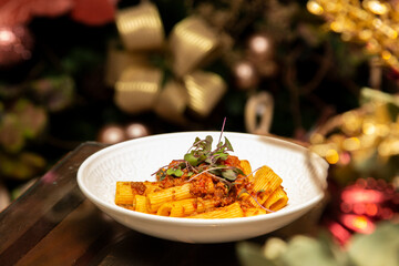 Rigatoni pasta with sugo sauce and lamb ragout, with coriander leaves on top. Christmas background.