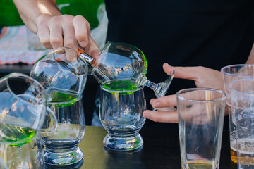 The bartender pours green absinthe into beautiful wine glasses and sets them on fire at a street party.