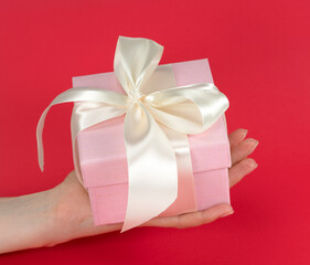 Woman's hand holding a gift with a yellow bow on a red background