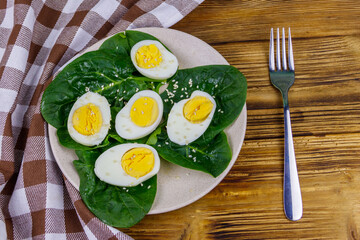 Boiled eggs with fresh spinach leaves and sesame seeds on wooden table. Top view