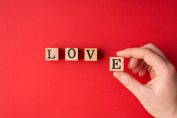 Top above overhead close up view photo of female hand putting wooden block on table surface making word love isolated bright vivid color backdrop