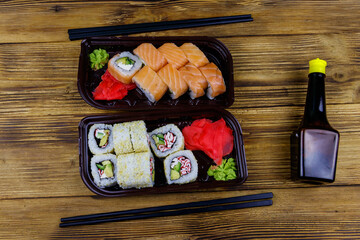 Set of sushi rolls in plastic boxes, soy sauce and chopsticks on wooden table. Top view. Sushi for take away or delivery of sushi in plastic containers