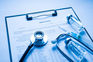 Close up photo of clipboard with stethoscope glass vial and syringe lying on doctors desktop