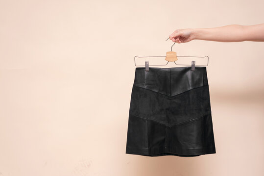 Woman is holding in hand a black skirt on the hanger on the light background.