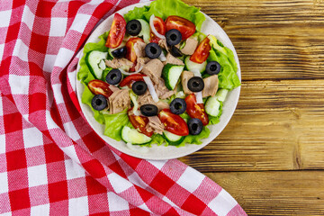 Tasty tuna salad with lettuce, black olives and fresh vegetables on wooden table. Top view