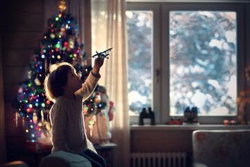 Little boy is playing with a plane near the new year tree. Image with selective focus.