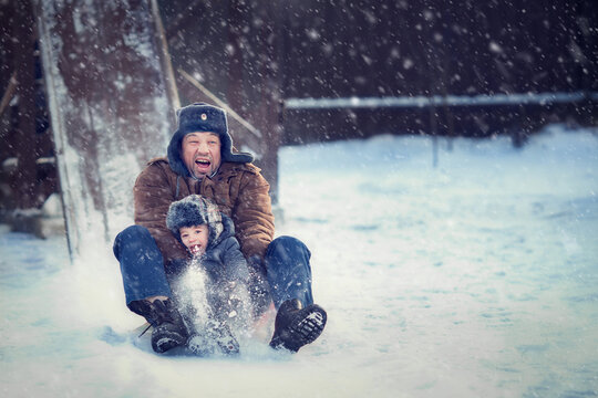 Father and his little son with very funny face expressions are sledding from the wooden hill in Russia. Image with selective focus and toning