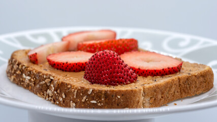 Peanut butter and strawberries on a slice of brown bread with shallow depth of field