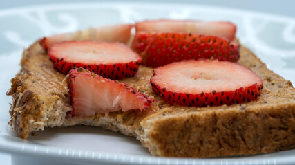 Taking bites off a slice of bread with peanut butter and strawberries