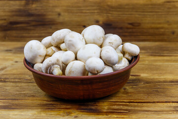 Fresh champignon mushrooms in ceramic bowl on the wooden table