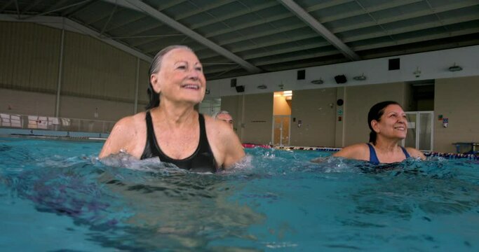 Seniors jumping with dumbbells water aerobics class in indoor pool