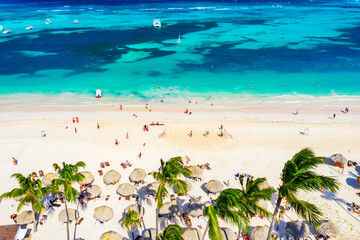 Beach vacation and travel background. Aerial drone view of beautiful atlantic tropical beach with straw umbrellas, palms and boats. Bavaro beach, Punta Cana, Dominican Republic.