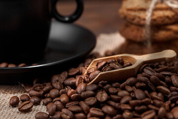 Close-up of a cup of hot drink on roasted coffee beans and oatmeal cookies on a wooden kitchen table on woven burlap with copy space to decorate the text