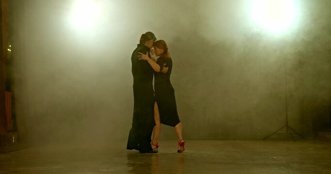 Woman and a man dance tango in a room with smoke, big lamps with light. Beautiful couple of professional dancers in the studio with smoke, romantic and passionate dance. 4k, ProRes