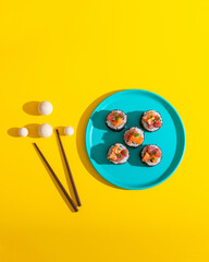 Abstract sushi roll on blue plate on yellow background with chopsticks