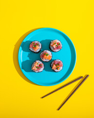 Abstract sushi roll on blue plate on yellow background with chopsticks