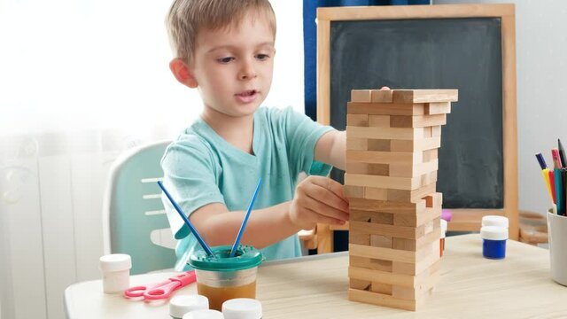 Smart boy pulling wooden blocks out of high tower made of bricks. Concept of smart children and home education during lockdown and self isolation.