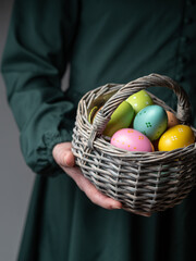 Close up of female in dark green dress holding basket of colored easter eggs. Easter concept. Dark...