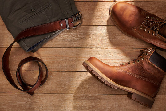 Leather men's boots and belt and jeans on wooden background. Fashion trend of casual style. Top view.